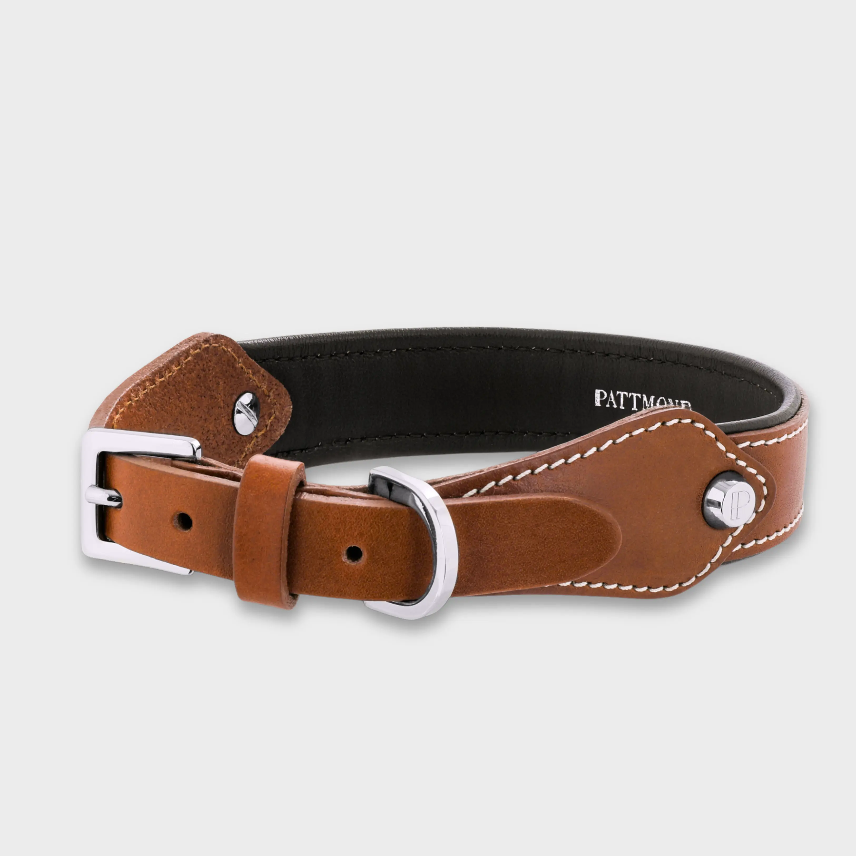 Hand-stitched from smooth, natural calfskin in an artisan workshop in the EU. Characterized by Pattmond’s signature shape, distinguished by subtle shifts in width and refined ornamental details. Caramel-coloured, vegetable-tanned leather exterior with beige contrast stitching and a brown leather lining. Solid brass hardware in silver (D-ring for the leash, buckle and signature logo studs), nickel-free and protected with a durable, polished finish. Adjustable length (see dimensions to choose the best fit for your dog). Available individually or in a set with a matching leather leash and gloves (made from lambskin).