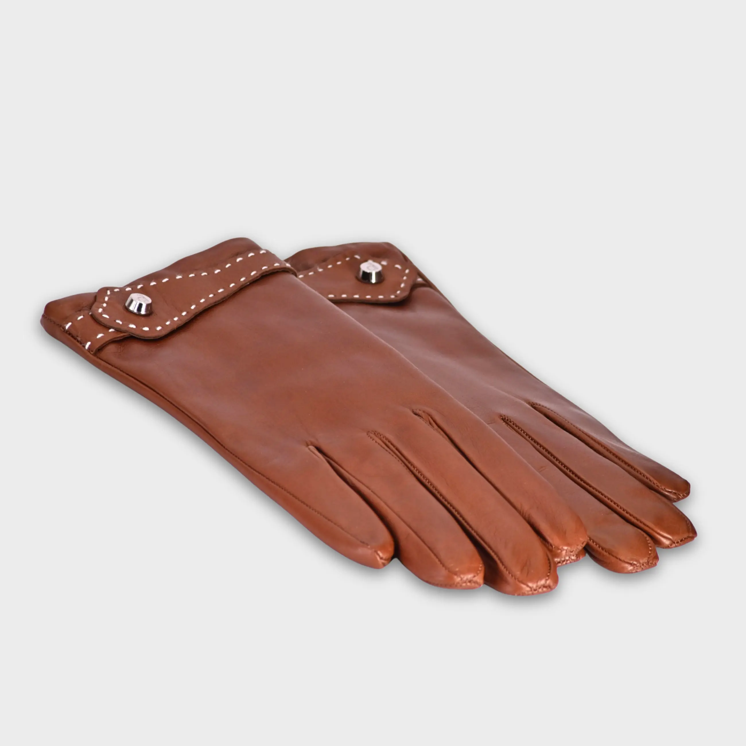 Handcrafted from smooth caramel lambskin and lined with natural beige cashmere. Finished with a decorative, hand-stitched leather strap in contrasting beige thread. Featuring the signature brass logo closure in silver, nickel-free and protected with a durable, polished finish. Made in an artisanal workshop in Italy. Available in sizes 7, 7.5, 8, 8.5, 9, 9.5 (Italian sizing).